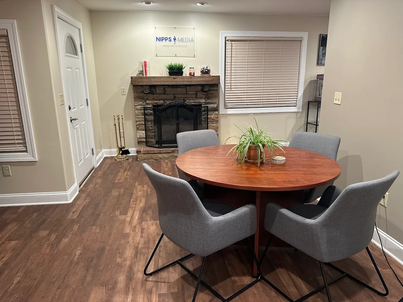 The Nipps Media studio, a warm meeting space with a stone fireplace, conference table, and the Nipps Media Marketing & Training plaque on the wall.